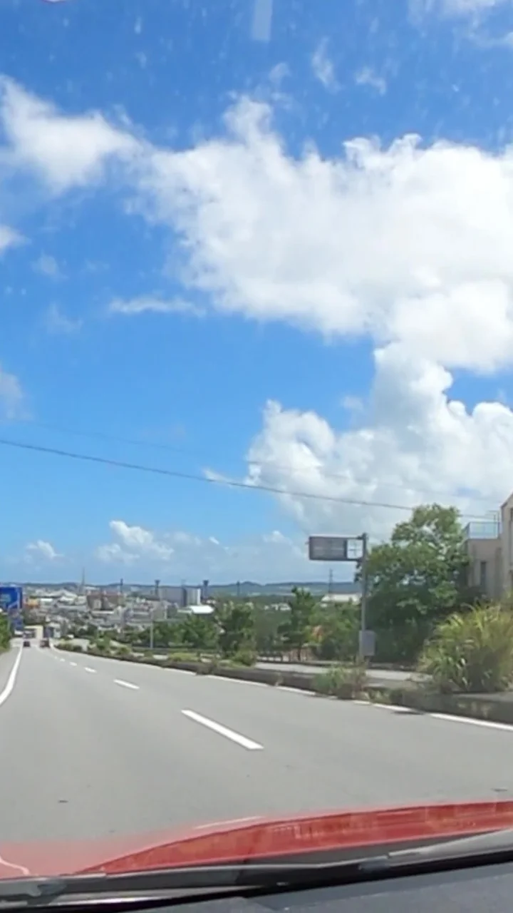 赤いBMWのボンネット越しに見える沖縄の道と青空