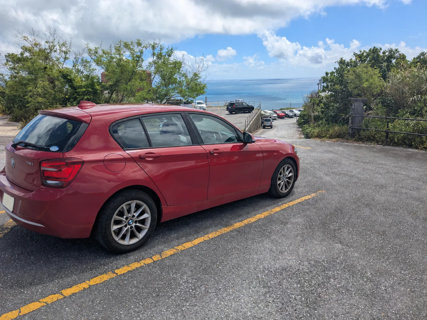 沖縄の海を背景に停めた赤いBMW F20